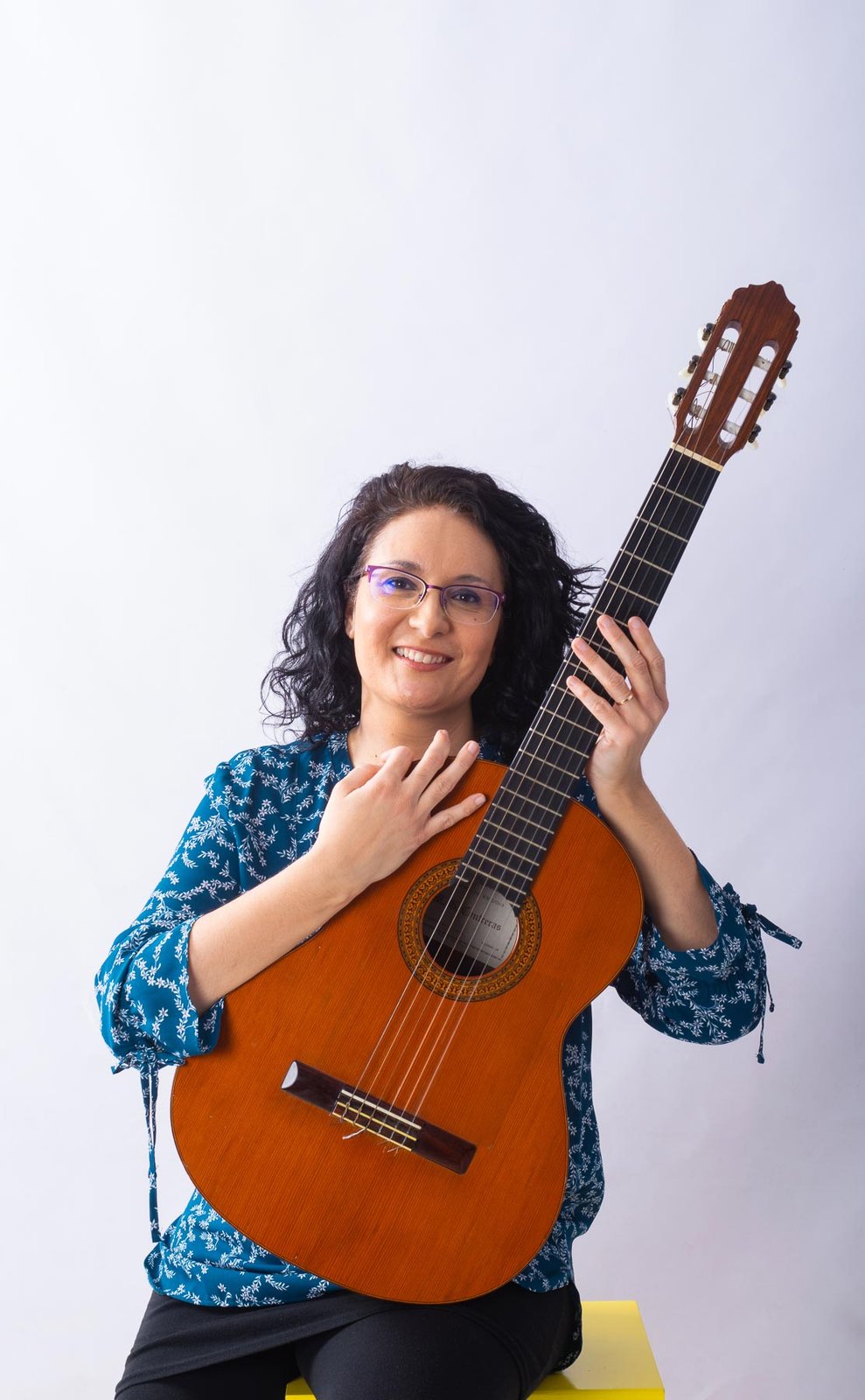 Mª Pilar García, sentada, abraza una guitarra española y sonríe a cámara.